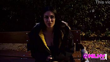 Aroused woman with large breasts contacts her former lover as an unknown person orally pleasures her in a public area.