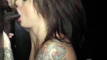 Brunette inked MILF with big boobs gives handjob and receives cum at gloryhole