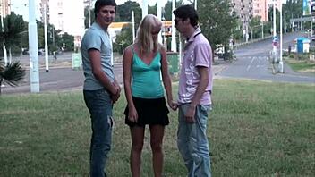 A blonde teen participates in a public group sex session with well-endowed men