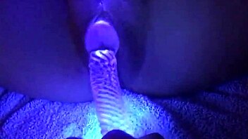 Illuminated nude woman using dildo