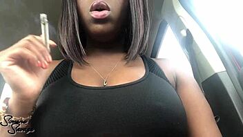 An ebony woman smokes a cigarette in the car.
