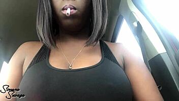 An ebony woman smokes a cigarette in the car.