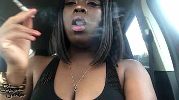 An ebony woman smokes a cigarette in the car.