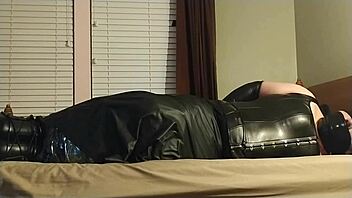 the crossdresser ties himself up in leather bondage, choking and gagging with boots