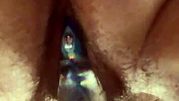 Close-up view of hairy pussy getting worked by a glass dildo in solo play.  