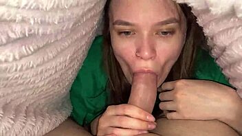 In the cozy bedroom, a young brunette girlfriend climbed under the blanket to deliver a deep blowjob to her roommate